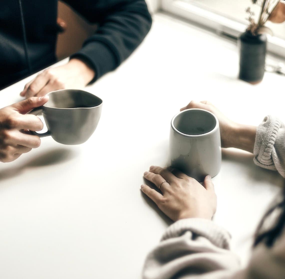 Two people with mugs at a sunlit table